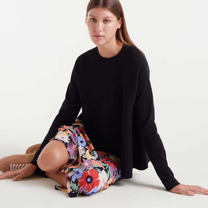Woman wearing a black sweater and colorful pants sitting on a white floor.