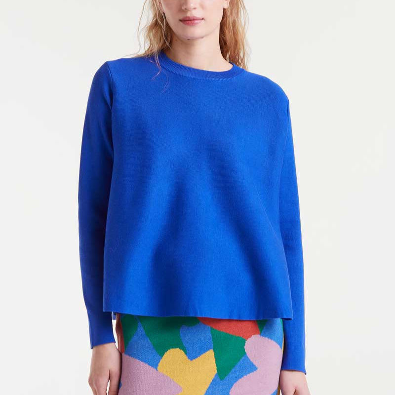 Person wearing a blue sweater with a colorful skirt on a white background