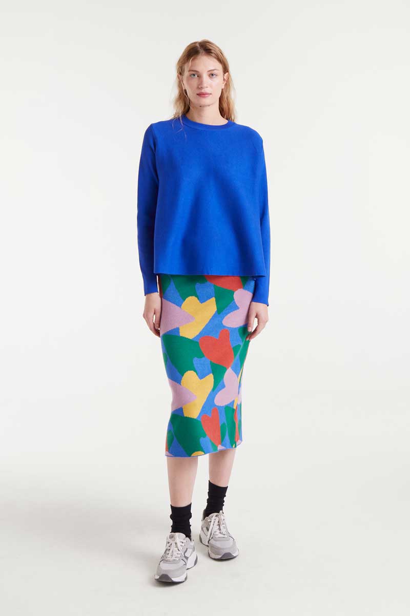 Person wearing a blue sweater and colorful skirt on a white background
