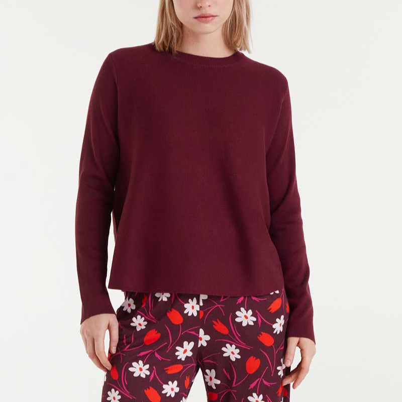 Woman wearing a burgundy sweater and patterned pants on a white background