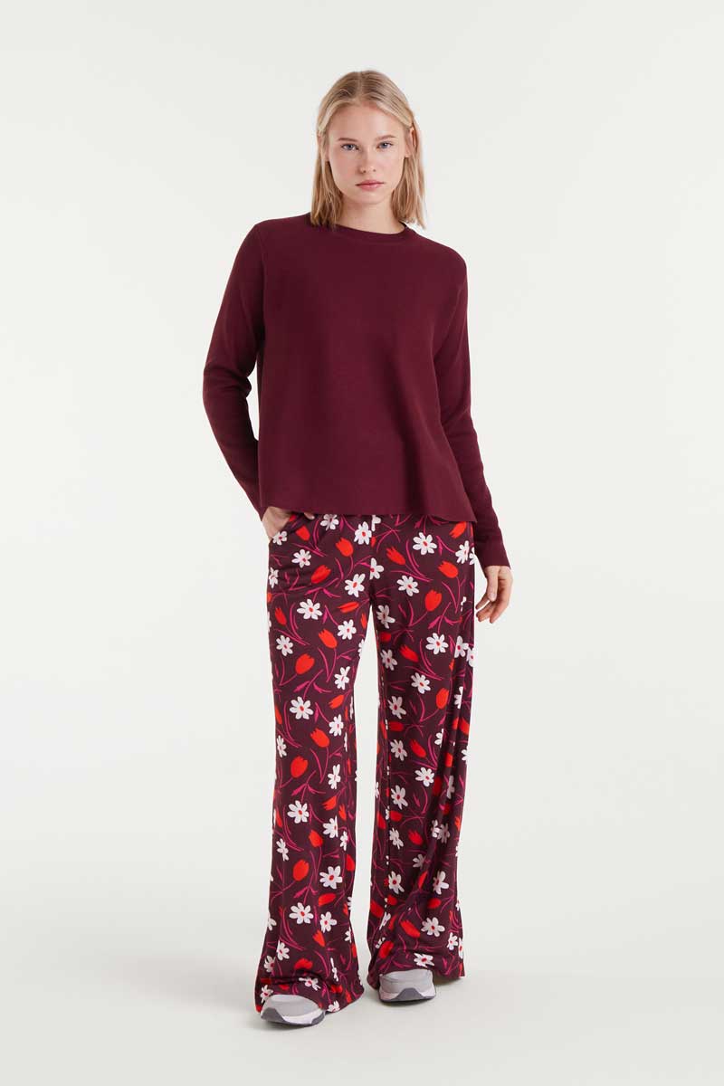 Woman wearing a burgundy sweater and floral-patterned pants on a white background