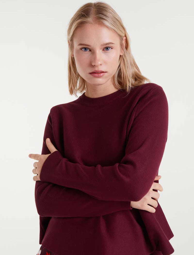 Woman wearing a burgundy peplum top with a plain background