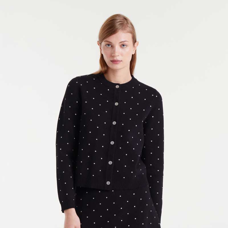 Woman wearing a black polka dot cardigan with a white background