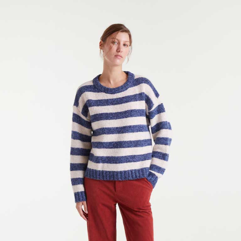 Person wearing a blue and white striped sweater with red pants on a white background