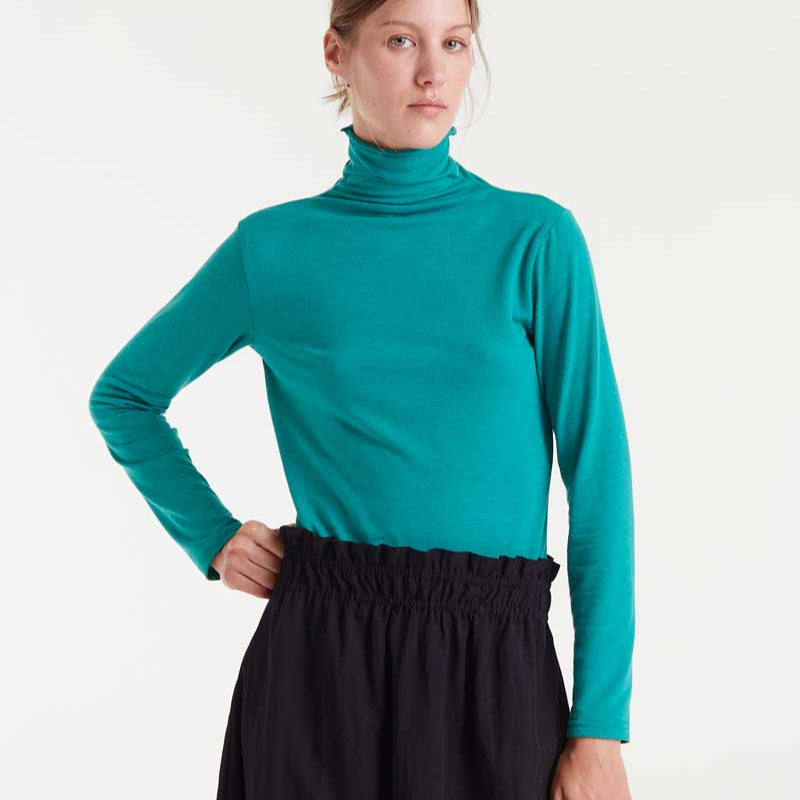 Woman wearing a teal turtleneck and black skirt on a white background
