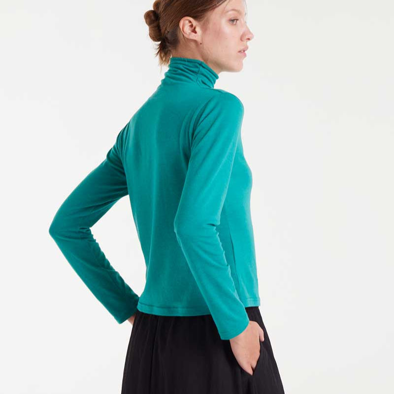 Woman wearing a teal turtleneck sweater and black skirt on a white background