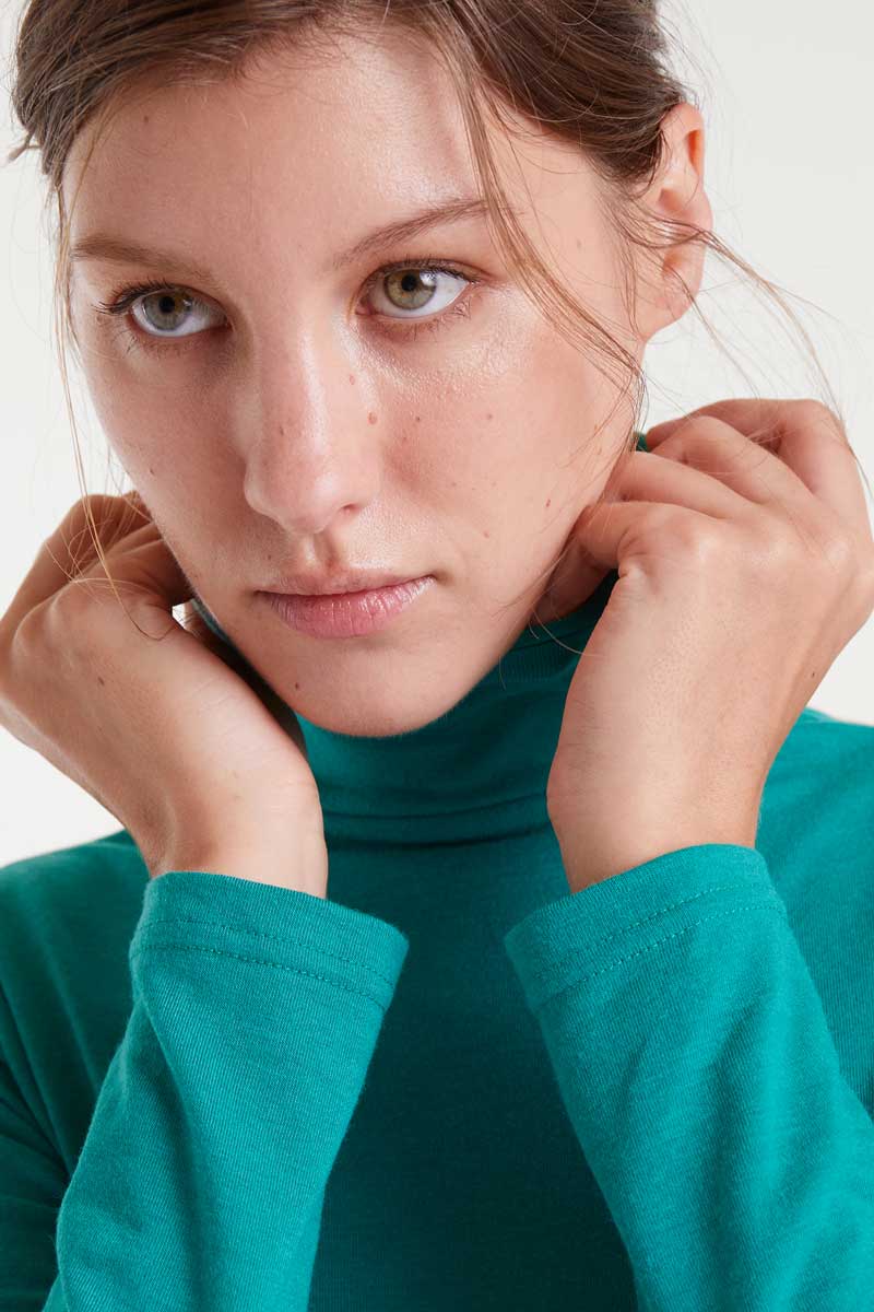 Woman wearing a teal turtleneck sweater with a neutral background