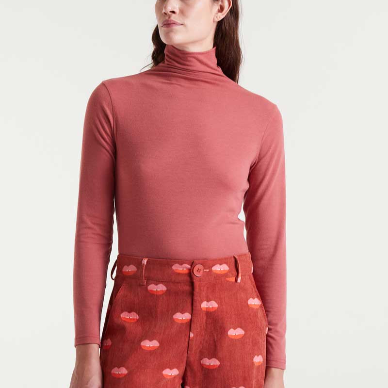 Person wearing a red turtleneck and patterned pants on a white background
