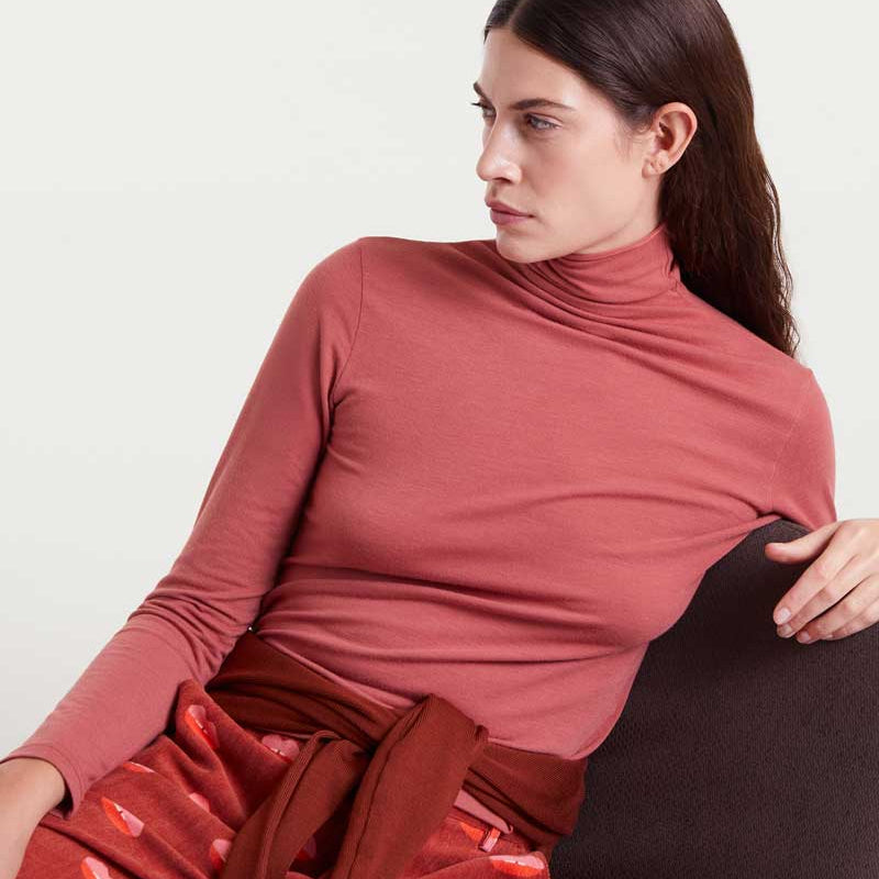 Woman wearing a red turtleneck and patterned pants sitting on a white background