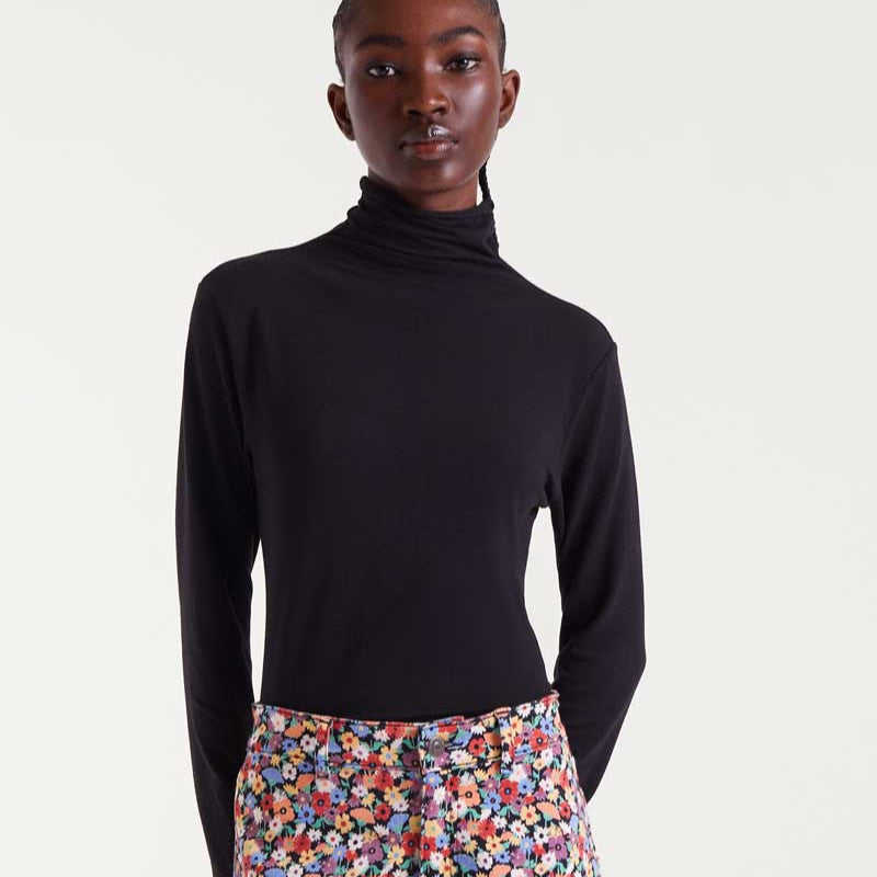 Person wearing a black turtleneck and colorful floral pants on a white background