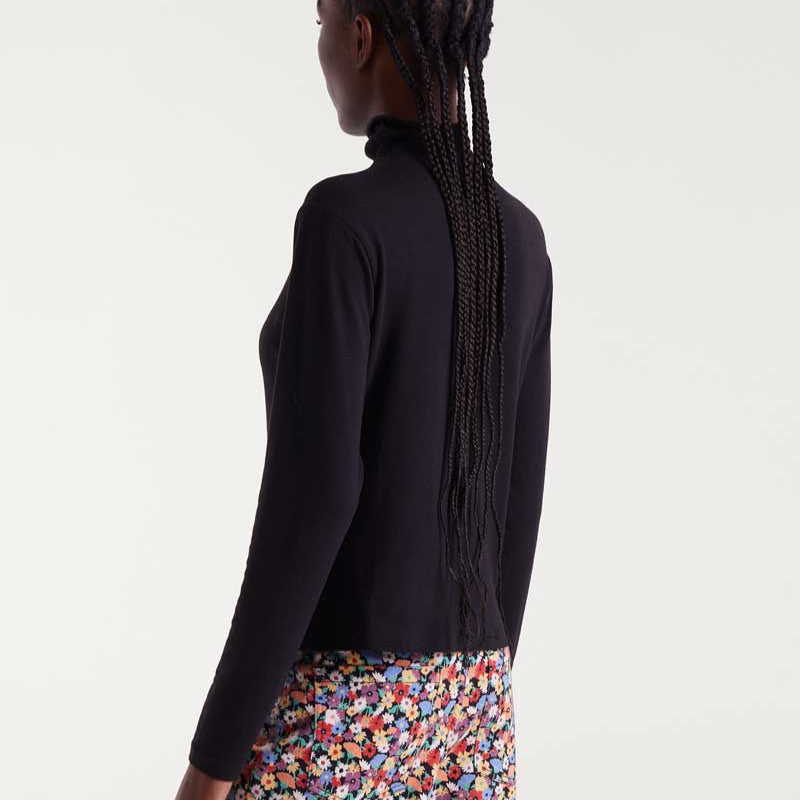 Person wearing a black turtleneck and colorful skirt on a white background