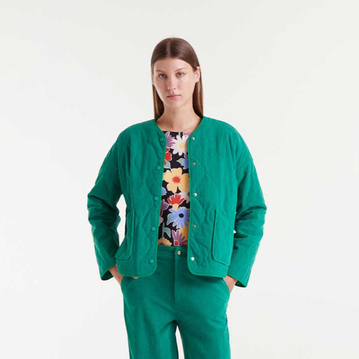 Woman wearing a green jacket and pants with a colorful floral top on a white background