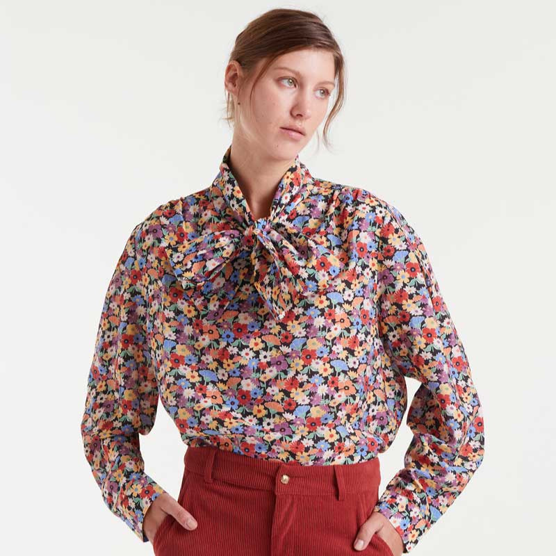 Woman wearing a colorful floral blouse with red pants on a white background