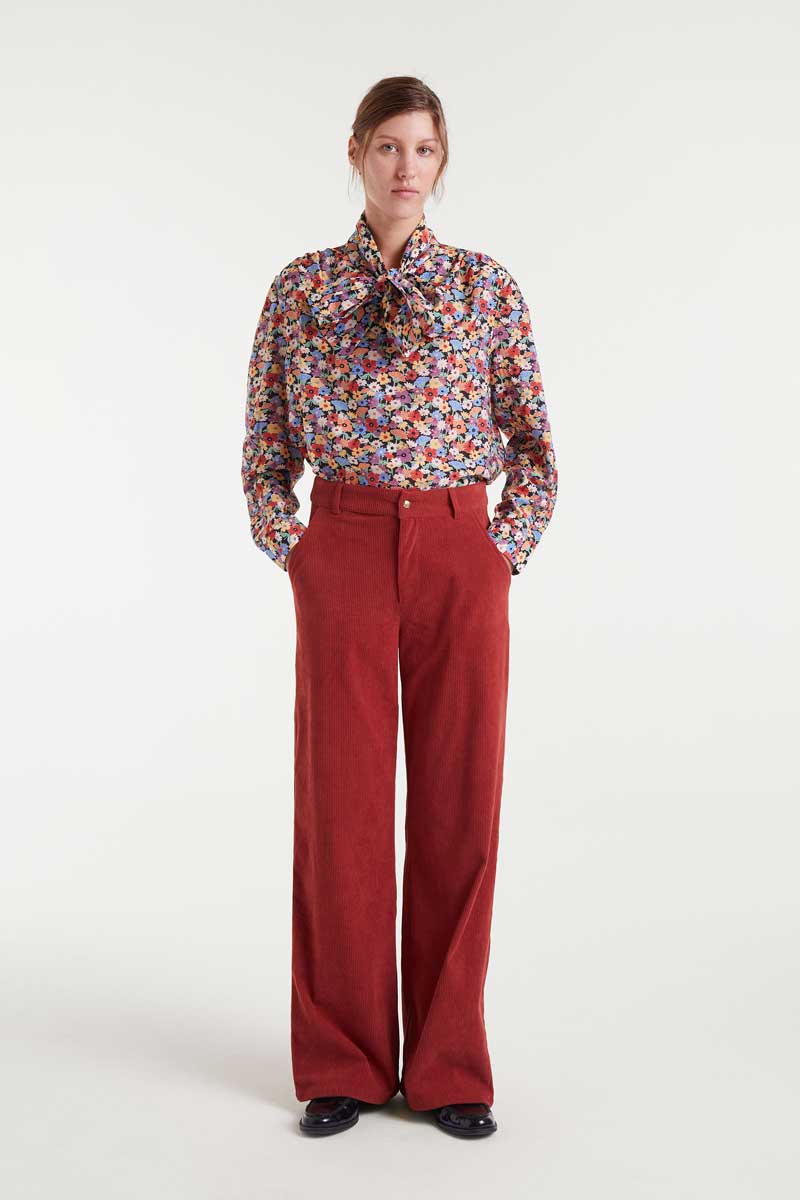 Woman wearing a colorful blouse and red pants on a white background