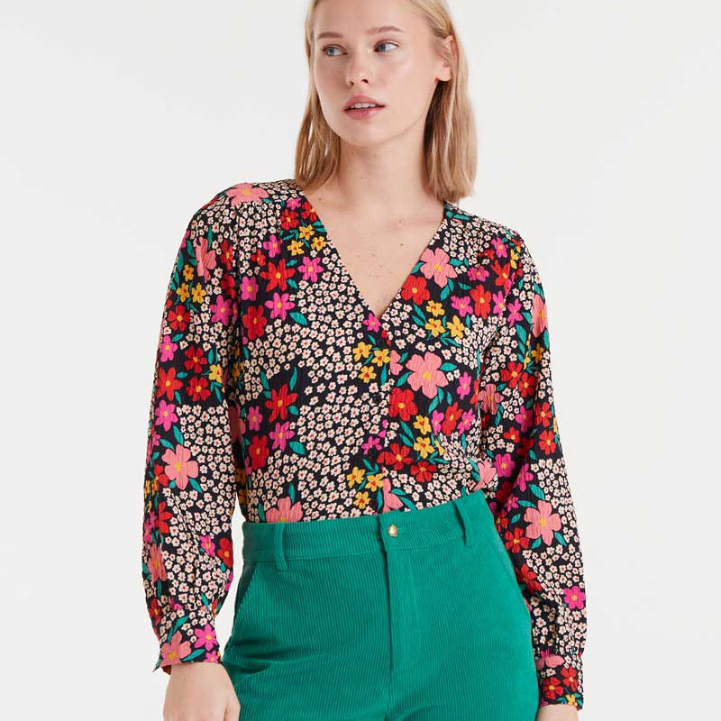 Woman wearing a colorful floral blouse and green pants on a white background