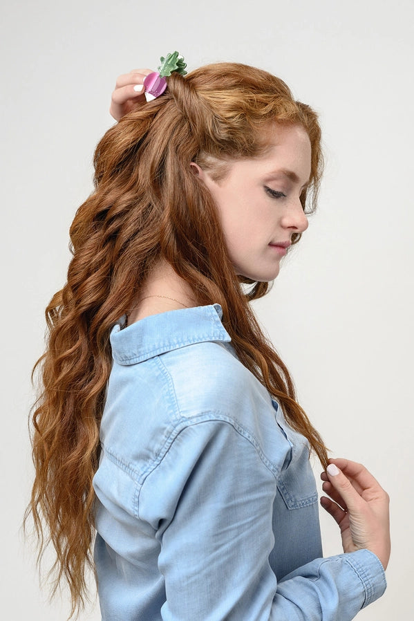 Woman with long, wavy hair styled in a side braid with a flower accessory, wearing a light blue denim shirt.