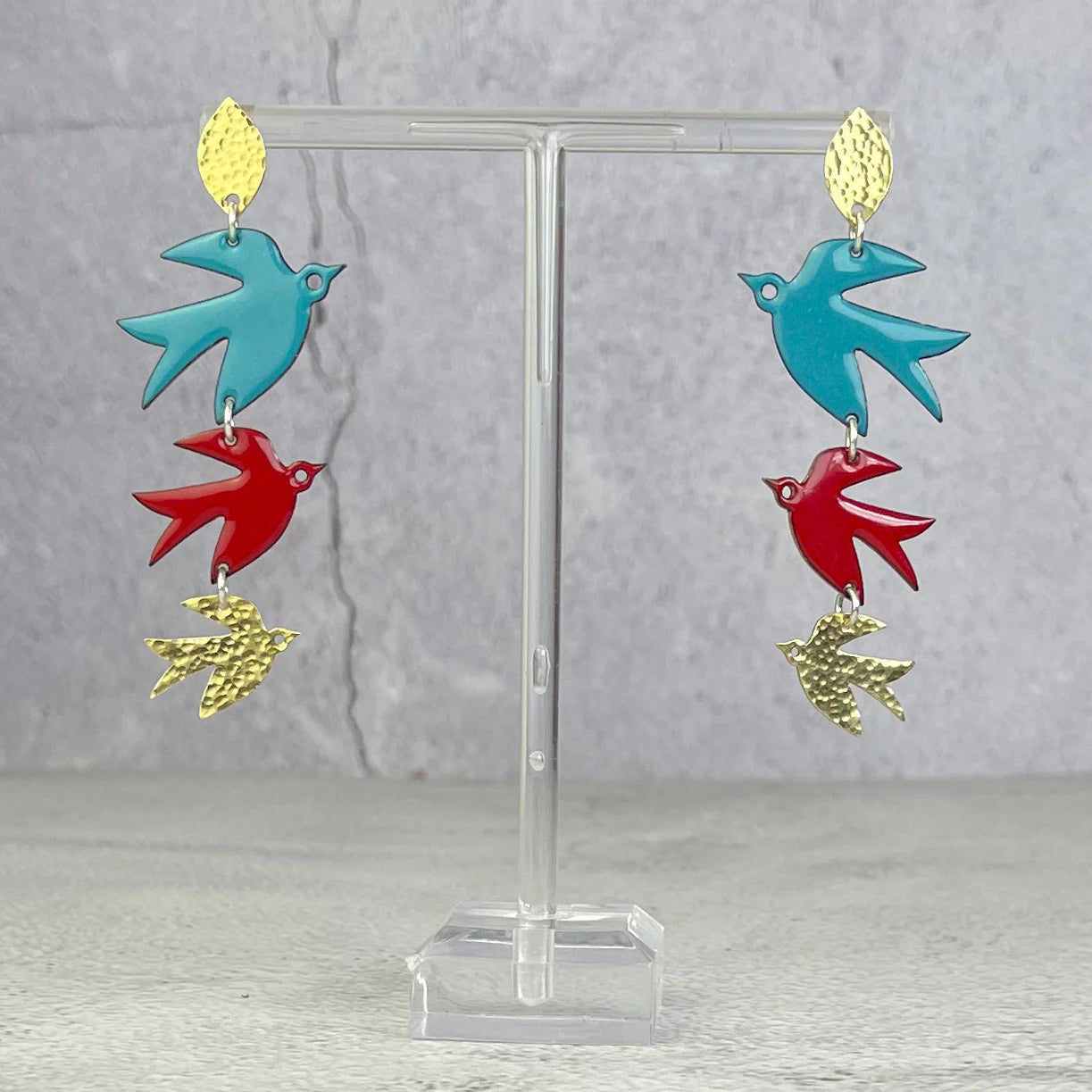 Colorful bird-shaped earrings on a clear stand against a gray background