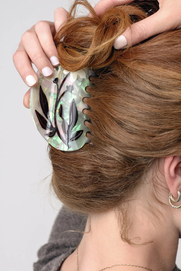 Person styling hair with a decorative hair bun holder featuring leaf patterns.