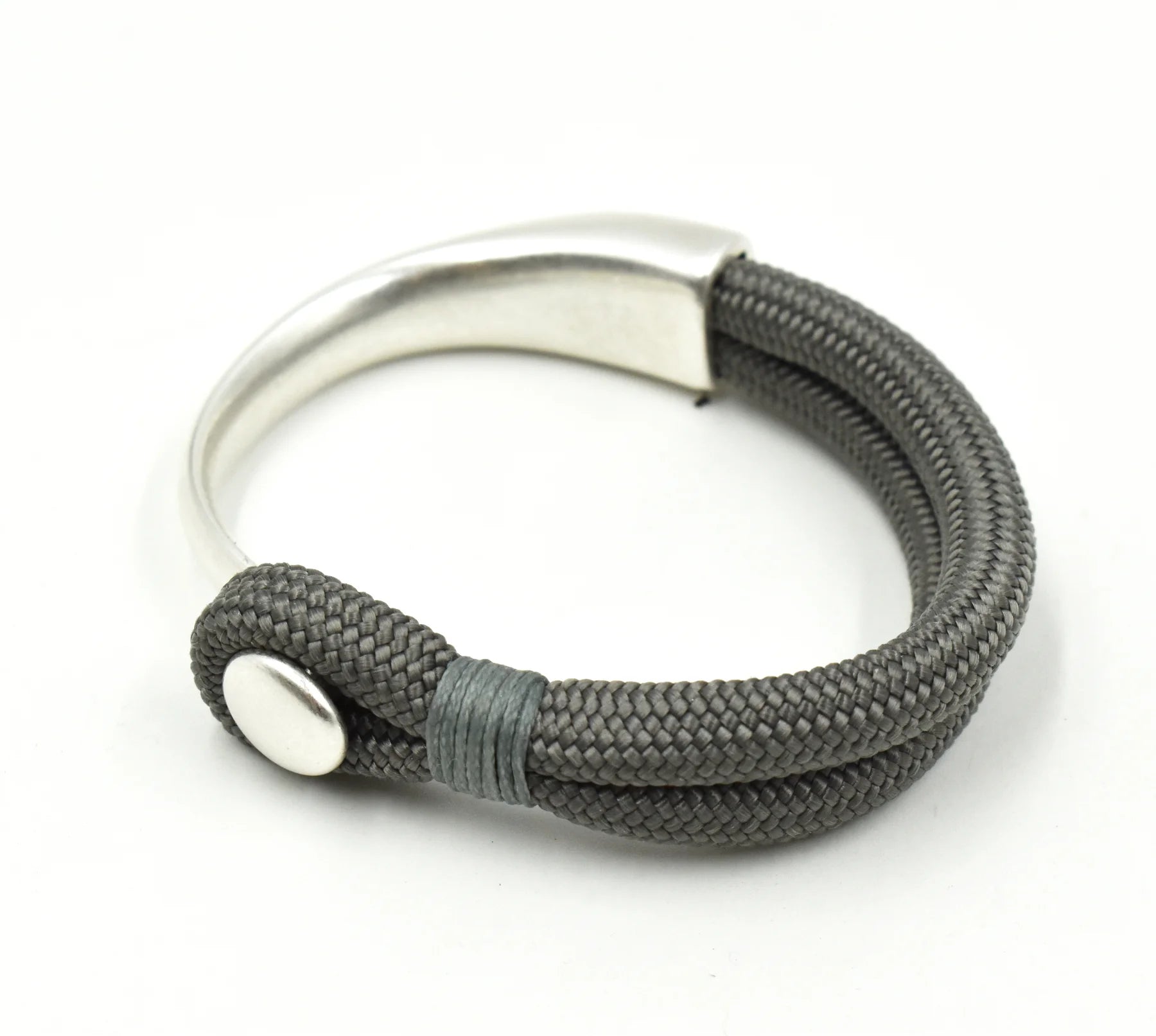 A silver-toned metal cuff bracelet with a thick, textured dark gray braided wrap, featuring a small round silver button closure on a white background.