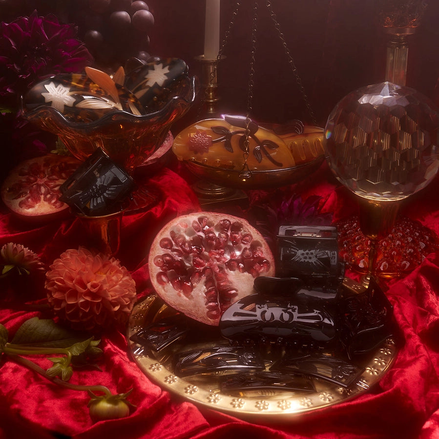 Decorative still life with pomegranate, chocolates, and flowers on a red cloth.