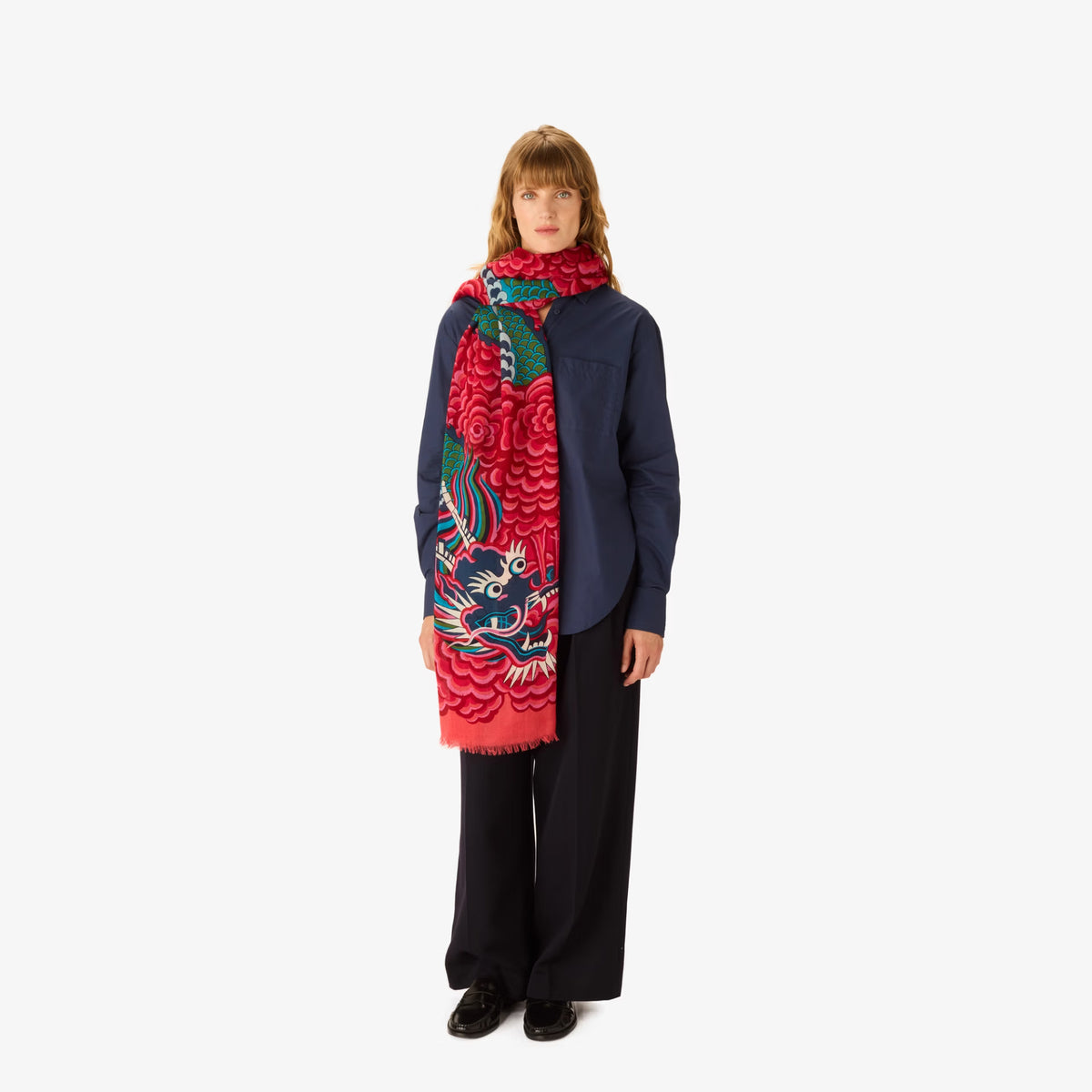 A model stands against a white background wearing a navy blue jacket, black wide-leg trousers, and a vibrant red scarf featuring a detailed multicolor dragon design.