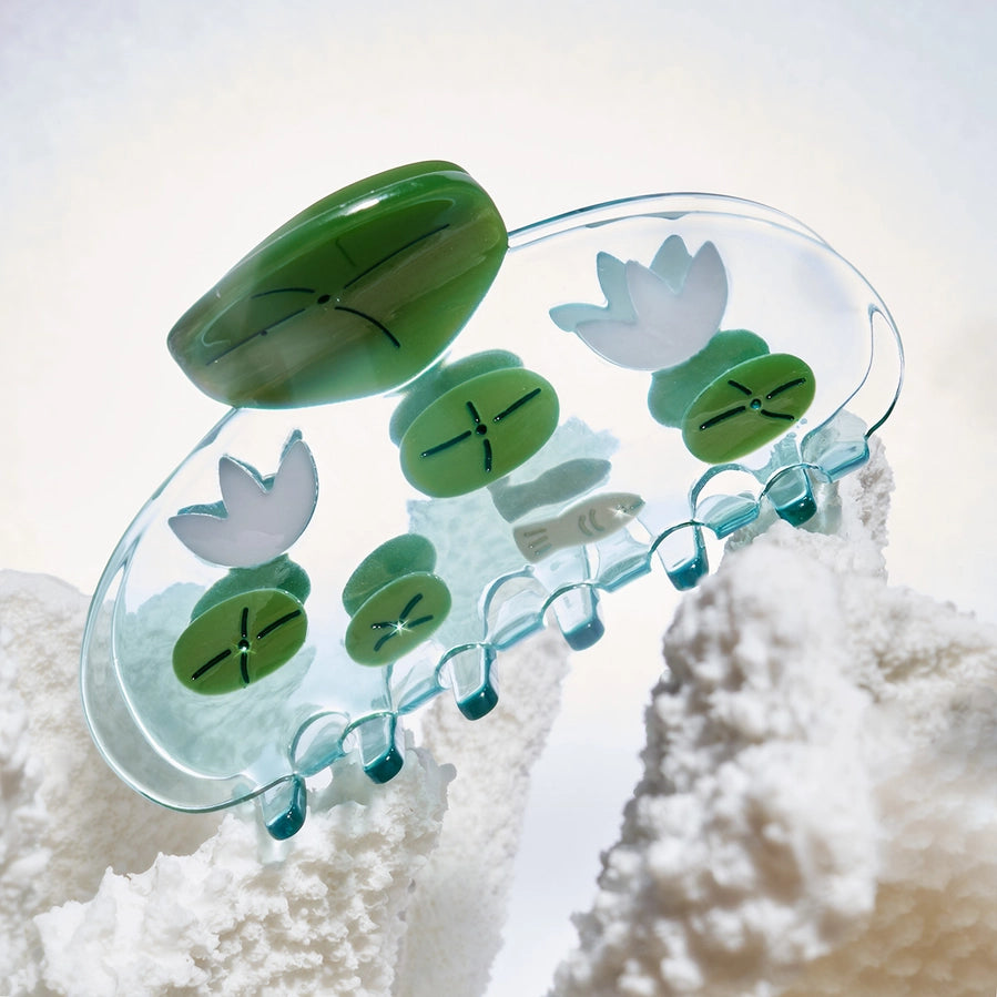 Decorative plastic hair clip with lily pads and fish on a textured white background