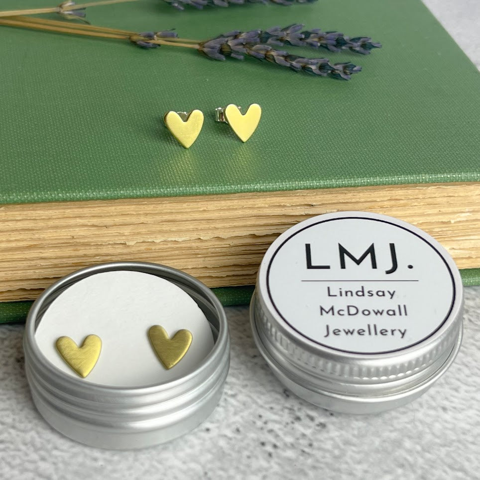 Pair of gold heart-shaped stud earrings in a silver tin.