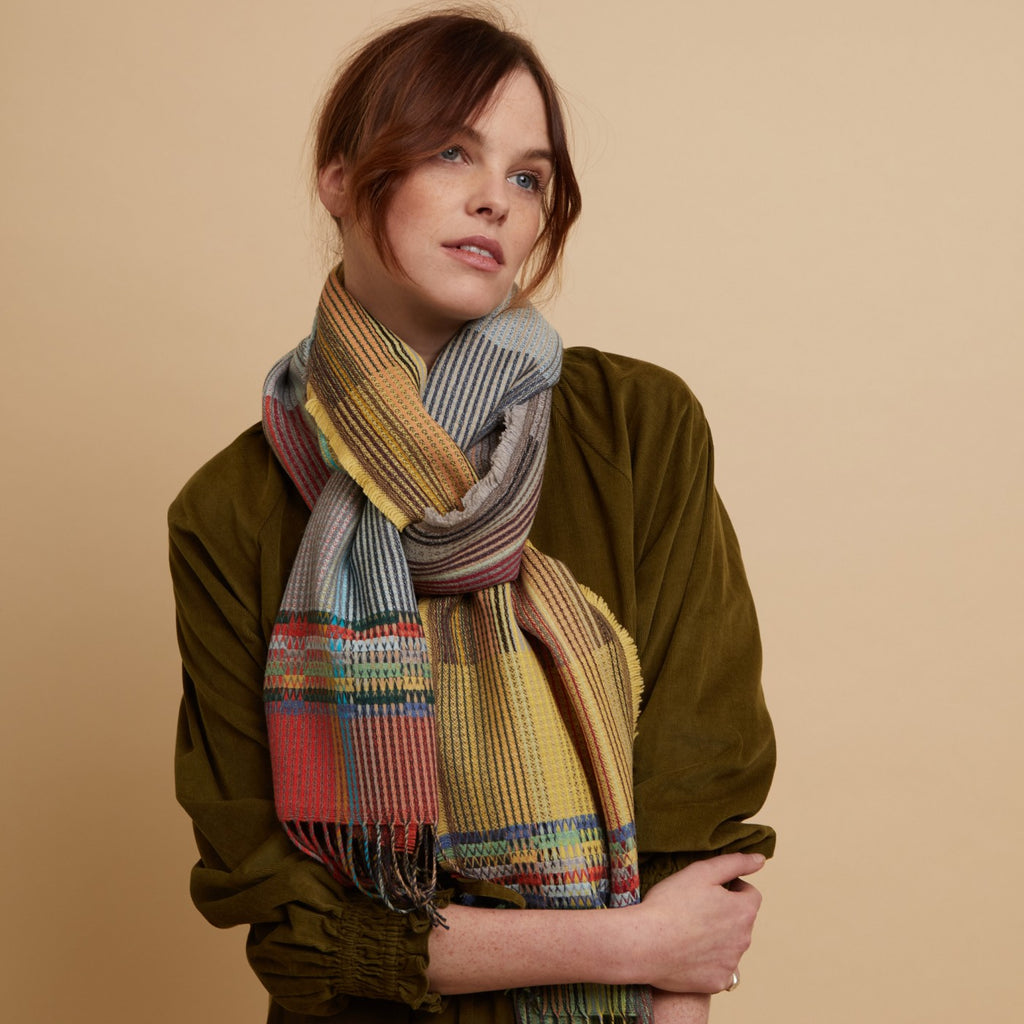 Multicolored woven scarf with fringe, featuring yellow, gray, red, and teal stripes and blocks.