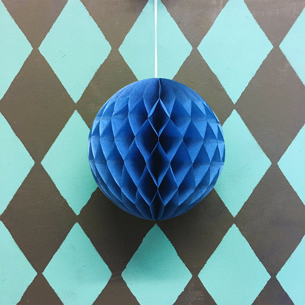 Dark blue honeycomb paper ball hanging against a teal and brown diamond patterned background.