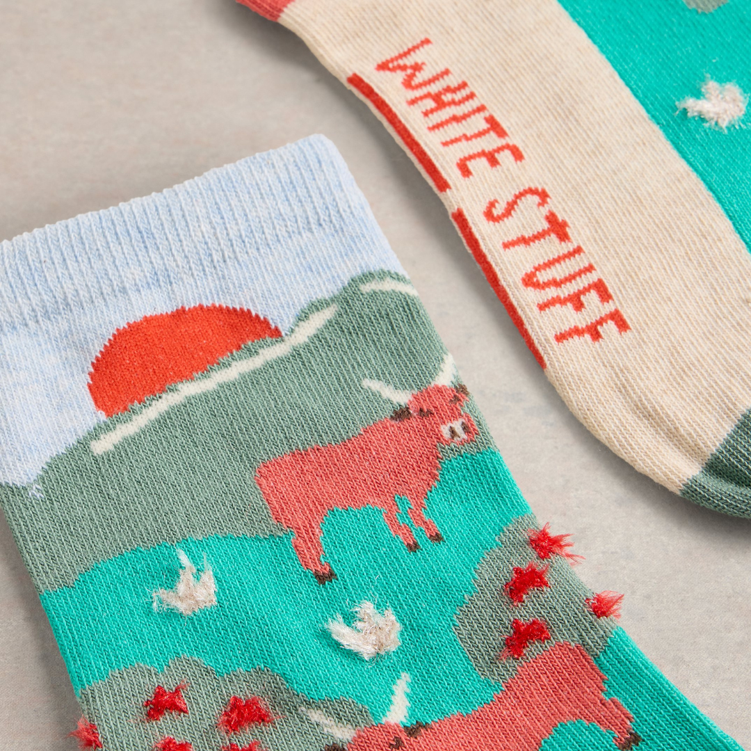 Pair of crew socks; one features a pastoral scene with a red cow, sunset, and birds; the other displays "White Stuff" text.