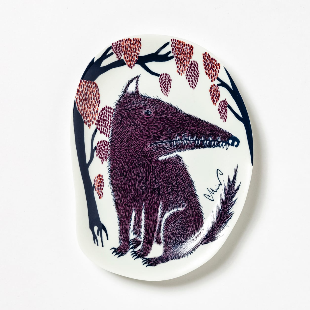 Decorative plate with a stylized wolf design and tree branches on a white background