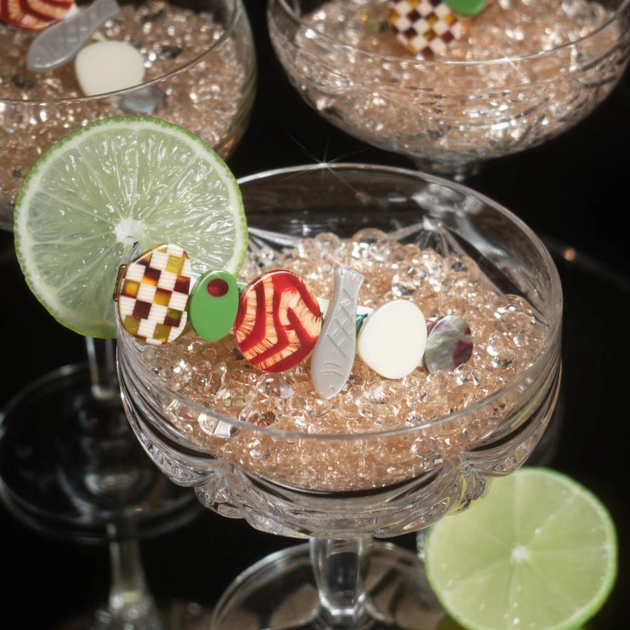 Food themed hair clips sit within a cocktail glass against a dark surface