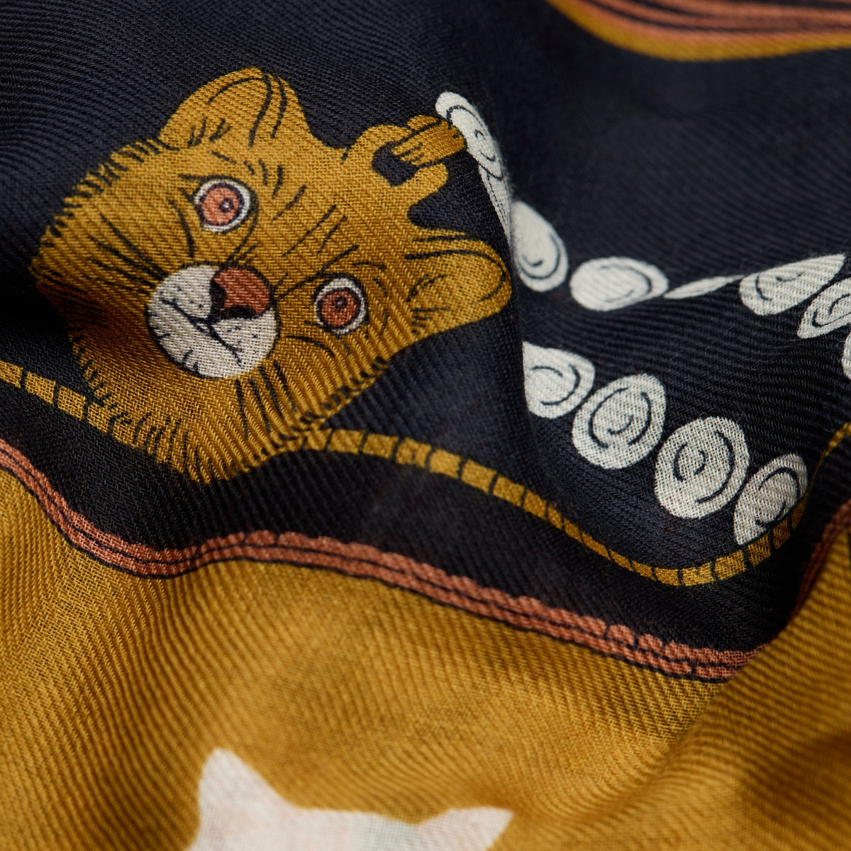 Close-up of a woven textile featuring a stylized yellow-orange tiger face on a dark navy background, with white circular motifs and a mustard yellow lower section.