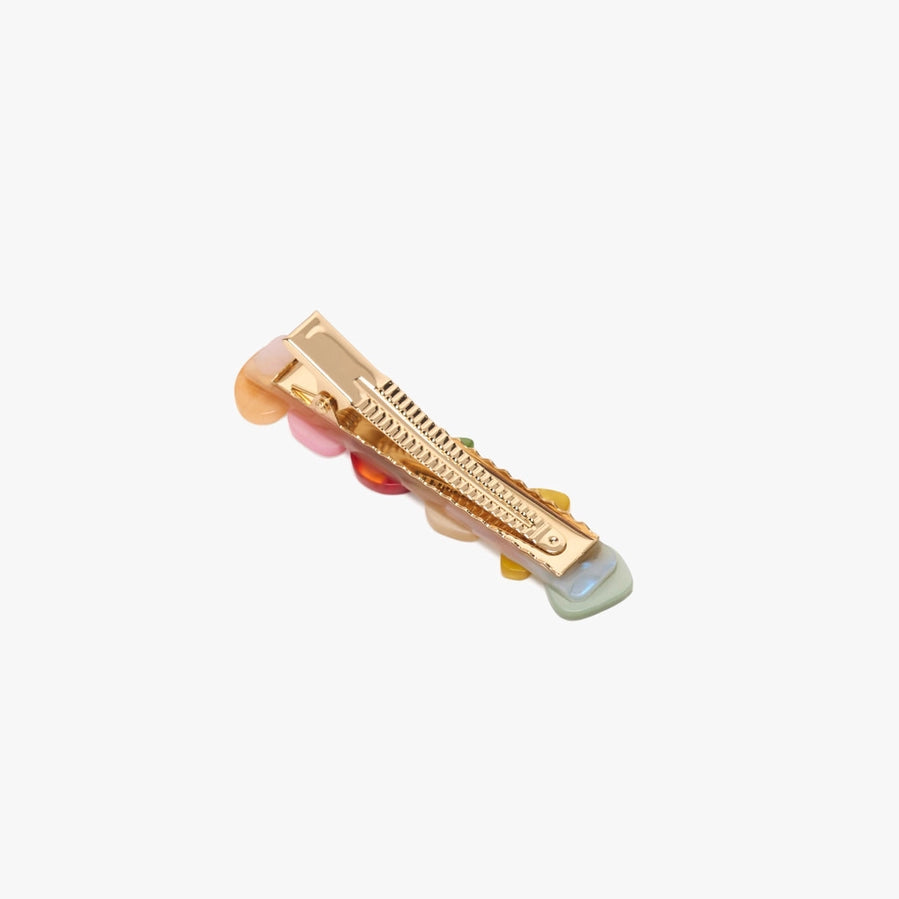 The reverse side of a gold hair clip with pink and green accents on a white background