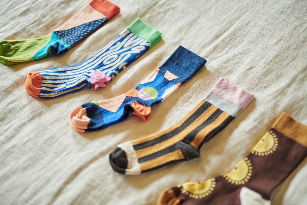 Five colorful patterned socks arranged diagonally on a textured beige fabric background.