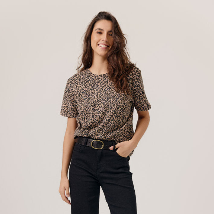 Woman wearing a leopard print top and black pants on a plain background