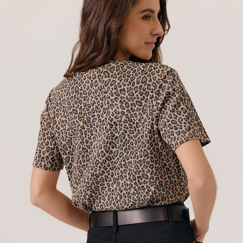 Woman wearing a leopard print top and black pants on a plain background