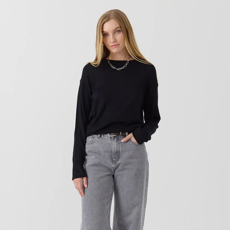 Woman wearing a black long-sleeve top and gray jeans on a white background