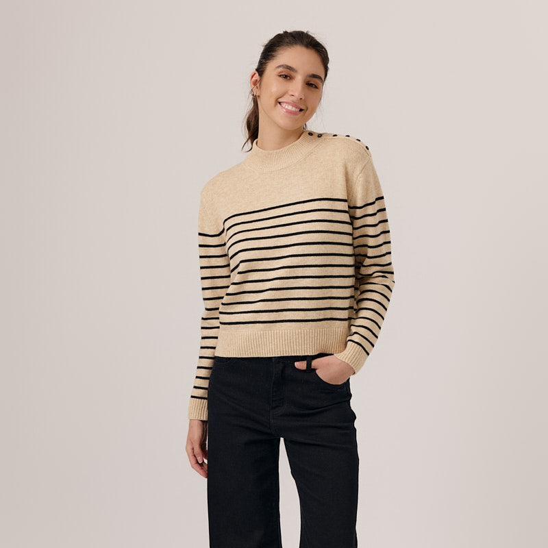 Woman wearing a beige and black striped sweater with black pants on a white background