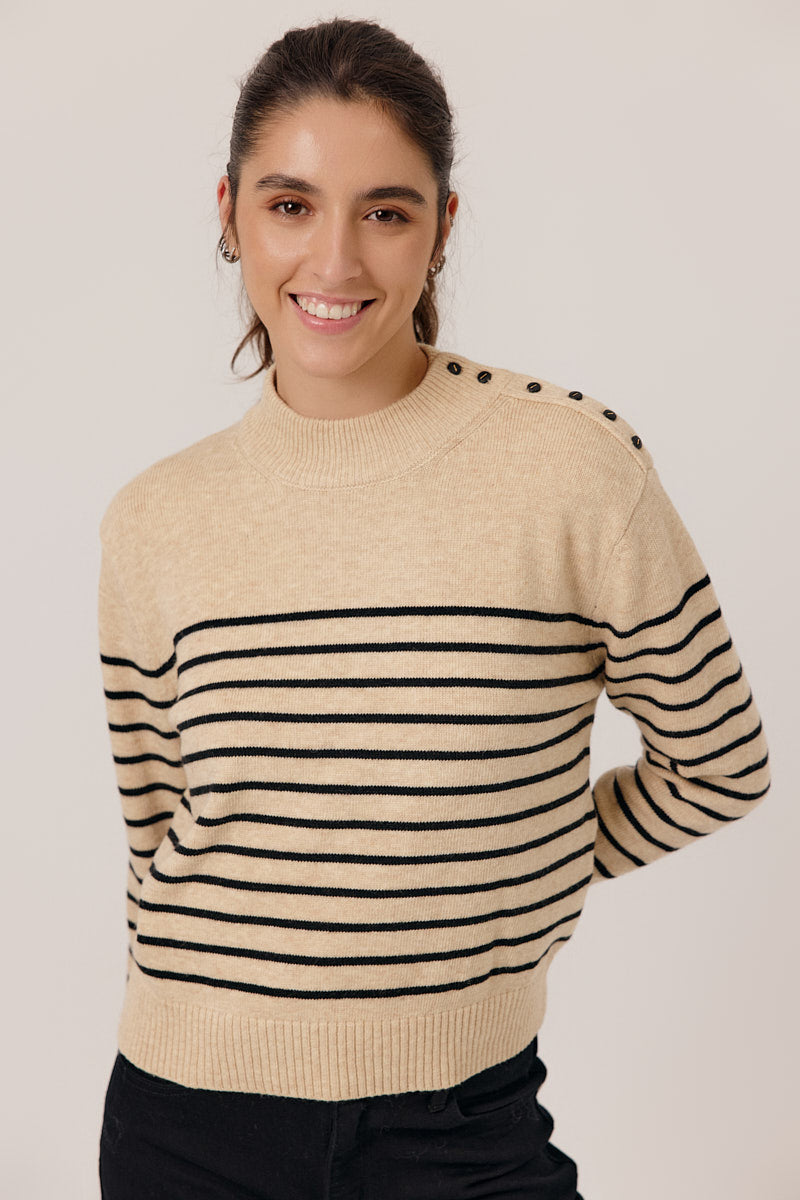 Woman wearing a beige sweater with black stripes on a plain background