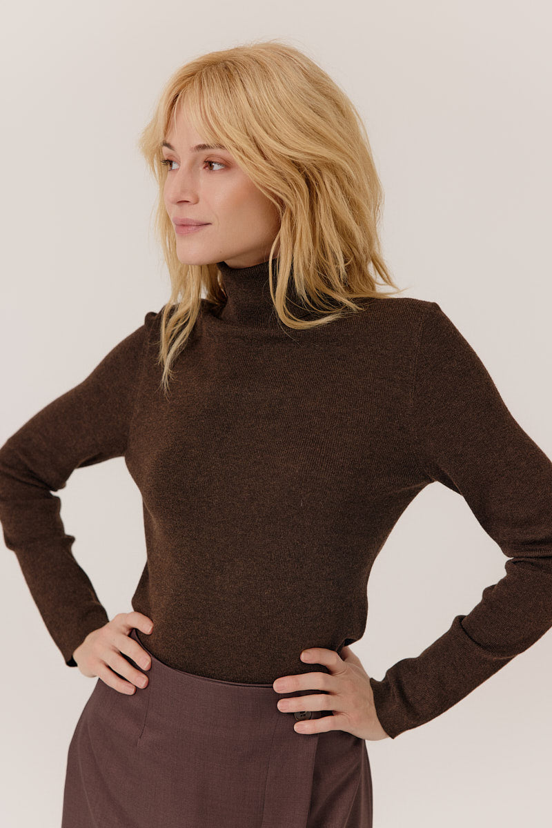 Woman wearing a brown turtleneck sweater against a plain background