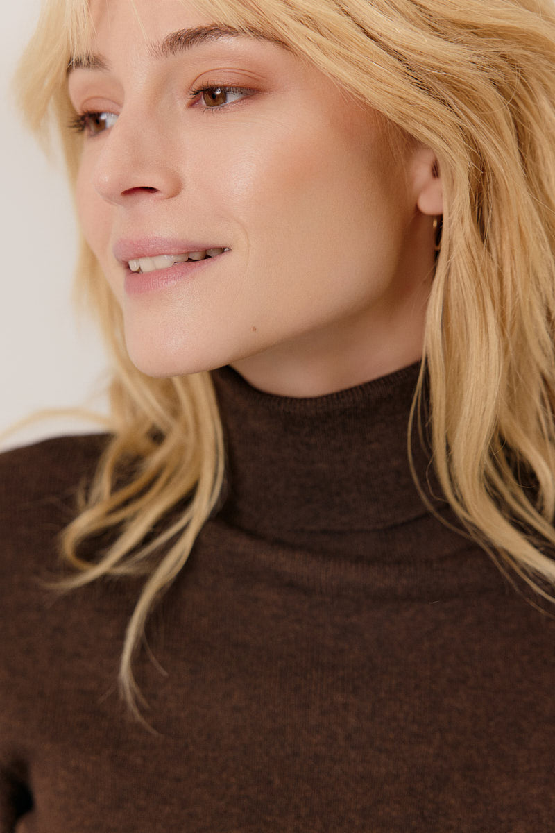 Close-up of a person wearing a brown turtleneck sweater with a neutral background