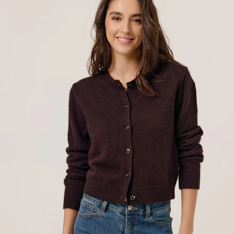 Woman wearing a brown cardigan and blue jeans against a plain background