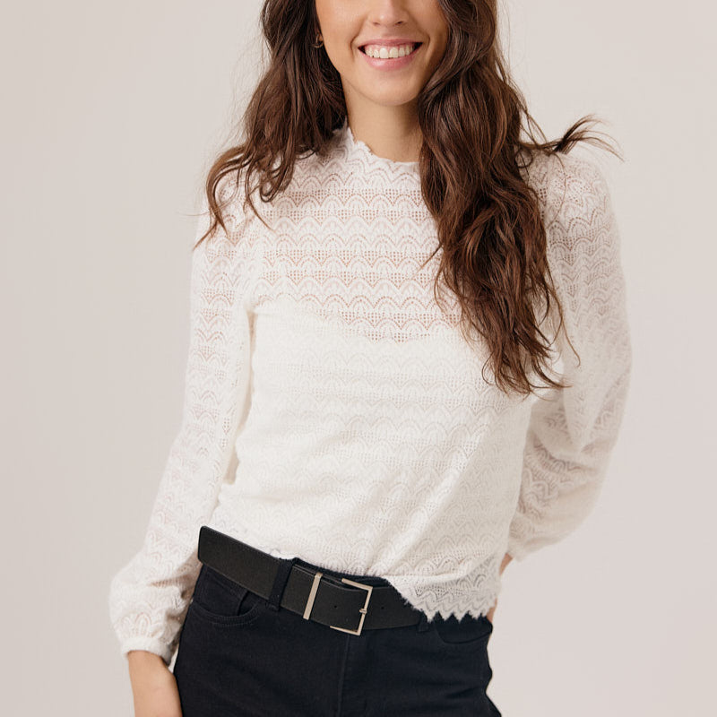 Woman wearing a white blouse and black pants against a plain background