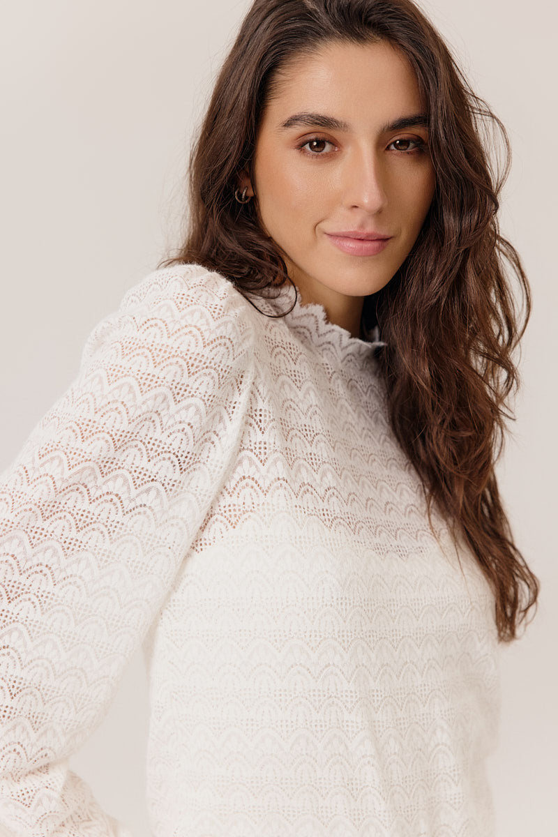 Woman wearing a white lace top against a plain background