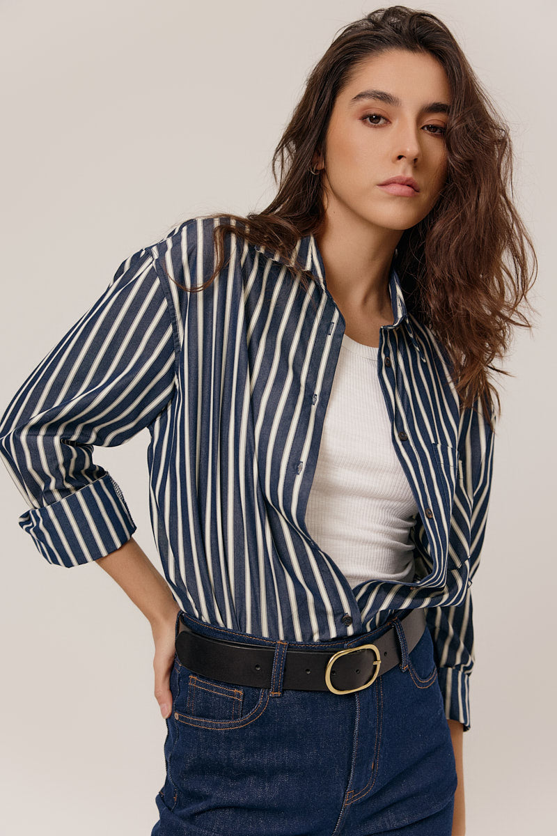 Woman wearing a striped shirt over a white top with blue jeans on a plain background