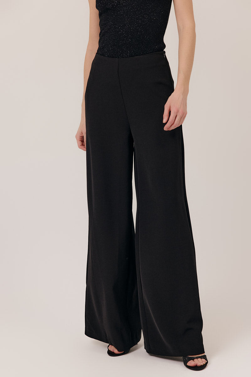 Person wearing black wide-leg pants and a black top on a plain background