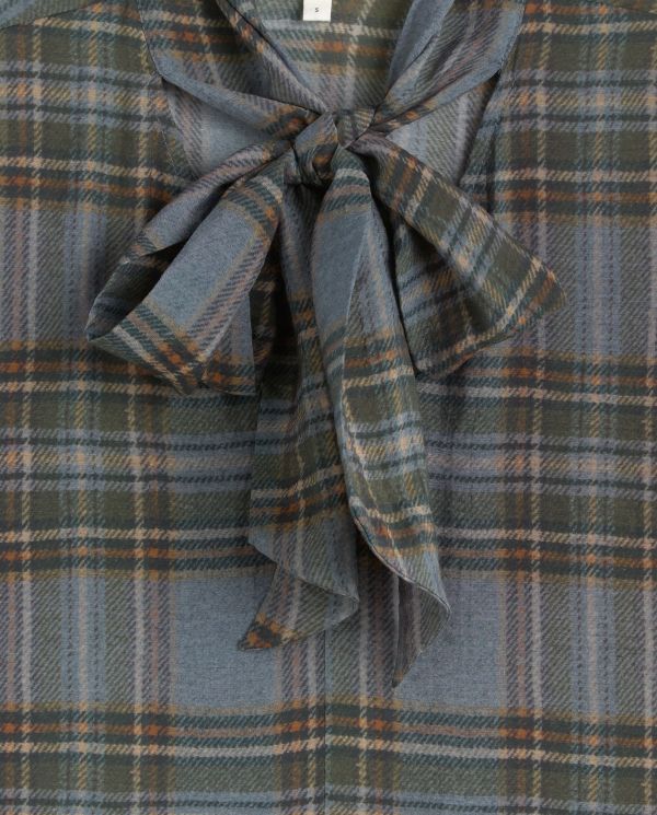 A close-up of a plaid fabric garment with a large bow detail at the neckline. The pattern is a muted blue-gray with olive green, brown, and thin white lines.