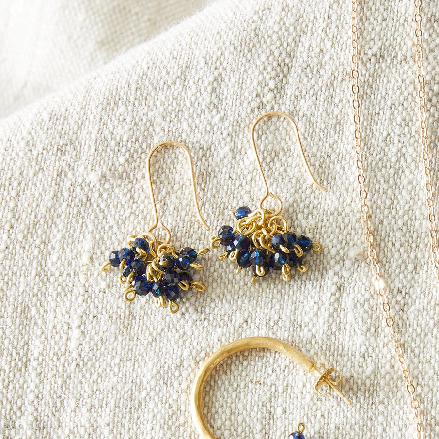 Gold dangle earrings featuring clusters of dark blue faceted beads.