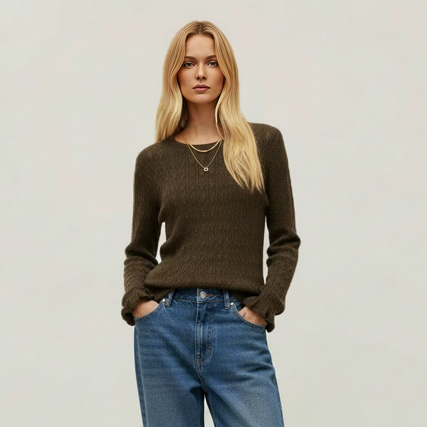 A woman stands against a plain light background wearing a dark brown ribbed knit sweater, blue cropped jeans, and dark brown slouchy knee-high boots.